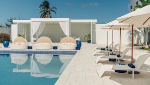 A pool area with lounge chairs and umbrellas, a clear blue sky, and palm trees.