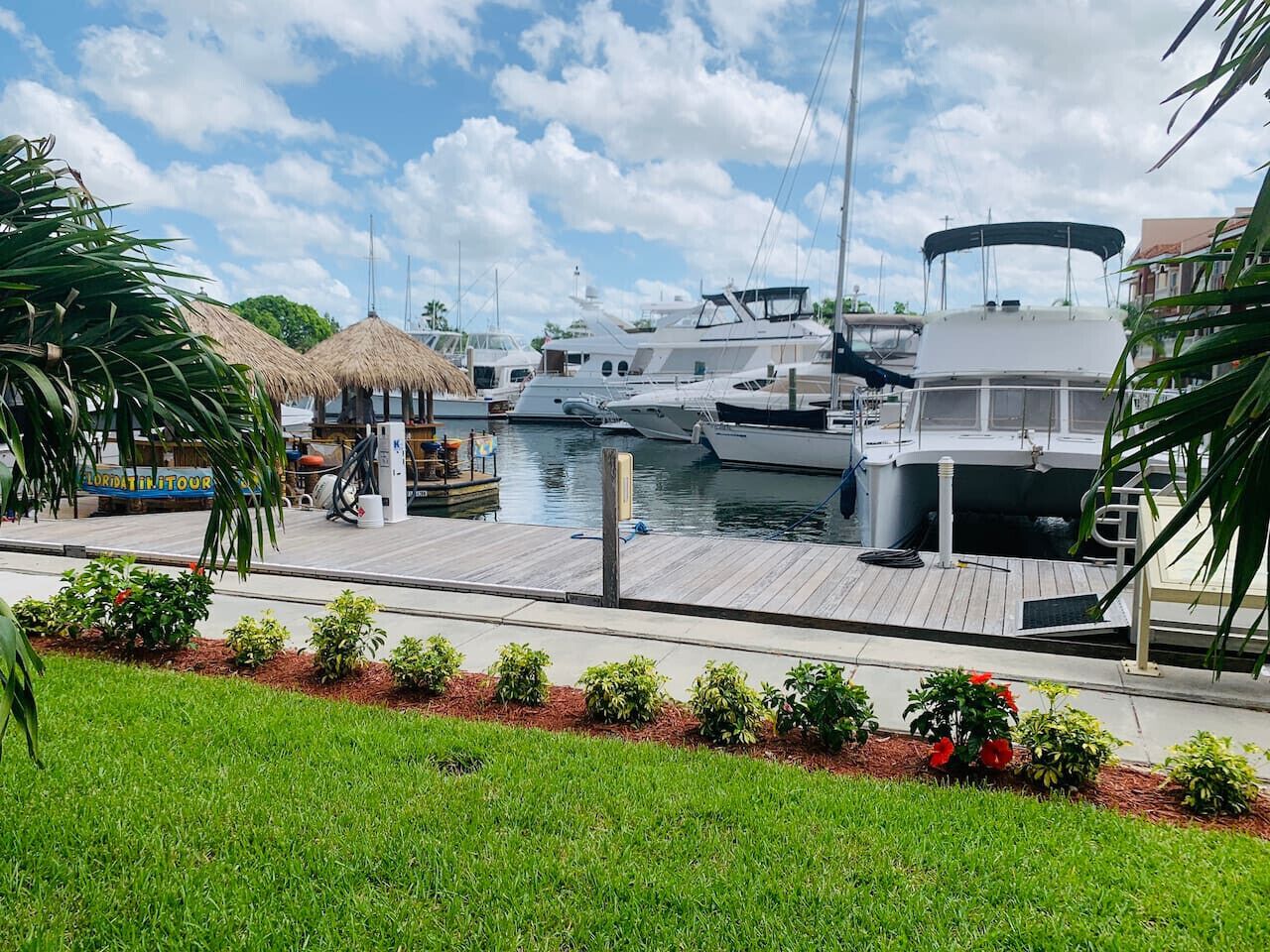 A marina with boats docked, a thatched-roof structure, and a well-maintained grassy area with small plants.