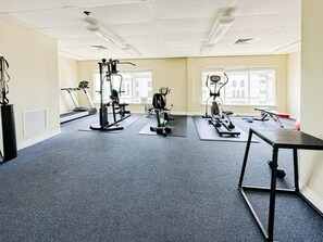 Een fitnessruimte met cardioapparatuur, krachtstations en een klein tafeltje.