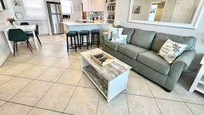 A modern kitchen with white cabinets, a stainless steel refrigerator, and a dining area with a table and chairs. - Paradise Awaits 250 Steps to Beach | Heated Pool (Saint Pete Beach)