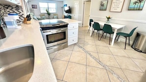 A modern kitchen with a central island, a dining area with green chairs, and a ceiling fan. - Paradise Awaits 250 Steps to Beach | Heated Pool (Saint Pete Beach)