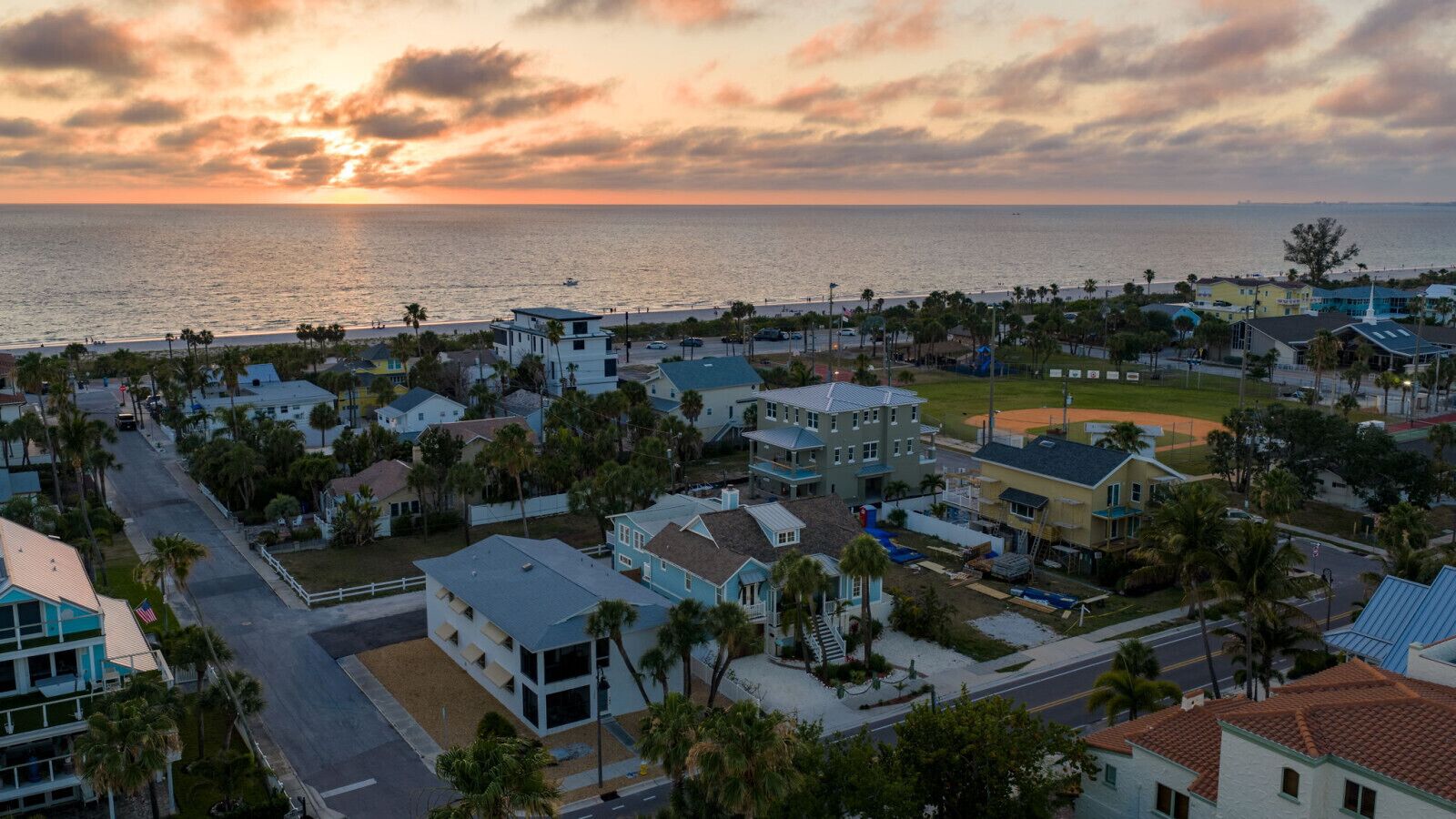 Zona residencial costera con casas, una carretera y vista al océano al atardecer.
