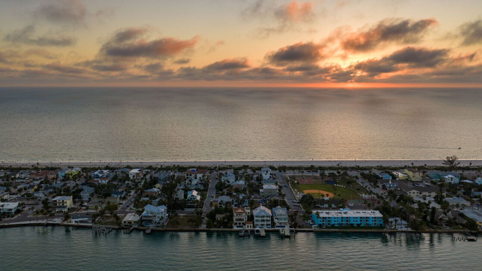 A coastal town with residential buildings, a marina, and a baseball field.