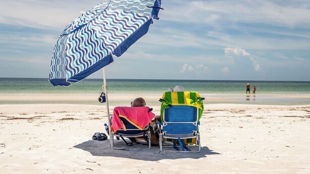 Zwei Liegestühle mit Handtüchern, ein Sonnenschirm und freie Sicht auf das Meer.