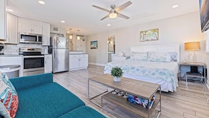 A modern hotel room with a kitchenette, a bed with a floral bedspread, a teal sofa, and a ceiling fan. - Beach-Goers Paradise Getaway! Pool! Sun! Fun! (St. Pete Beach)