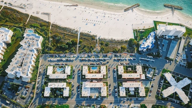 An aerial view of a coastal area with a beach, a parking lot, and modern buildings with a pool. - Beach-Goers Paradise Getaway! Pool! Sun! Fun! (St. Pete Beach)