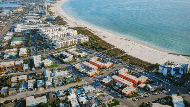 An aerial view of a coastal city with a beachfront, including residential buildings, a parking lot, and a beach with people. - Prime St Pete Beach Spot • Private Patio (St. Pete Beach)