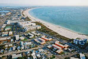 An aerial view of a coastal city with a beachfront, including residential buildings, a parking lot, and a beach with people. - Prime St Pete Beach Spot • Private Patio (St. Pete Beach)