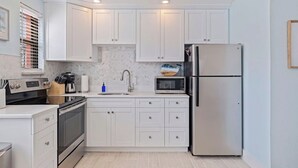 A modern kitchen with white cabinets, stainless steel appliances, and a tiled backsplash. - Prime St Pete Beach Spot • Private Patio (St. Pete Beach)