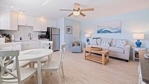 A modern kitchen with white cabinets, a dining area with white chairs, a wooden coffee table, and a living room with a grey sofa and blue lamps. - Prime St Pete Beach Spot • Private Patio (St. Pete Beach)