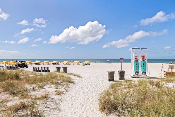 Une plage de sable avec des parasols jaunes, une tour de surveillance pour les sauveteurs et un ciel bleu dégagé.