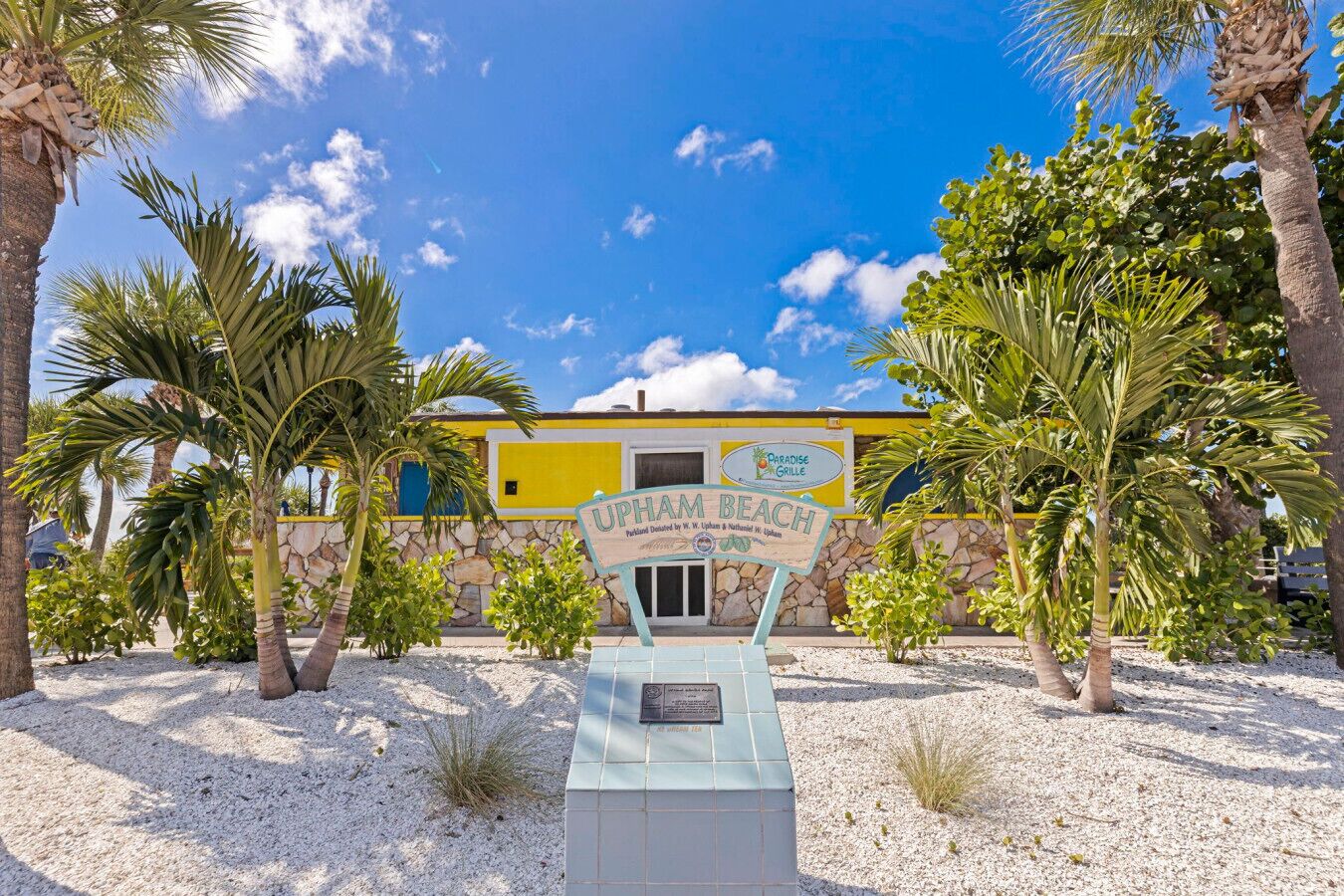 A sign for UPHAM BEACH with a building in the background.