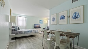 Une chambre à coucher avec un lit, une table à manger avec des chaises, un téléviseur et des œuvres d’art encadrées accrochées au mur.