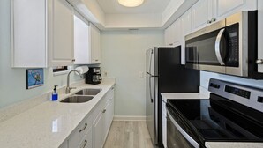Une cuisine compacte avec des meubles blancs, un évier en acier inoxydable, une machine à café, un four à micro-ondes, un réfrigérateur et un four.