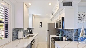 A modern kitchen with white cabinetry, a built-in oven, a microwave, and a sink. - Poolside Paradise with Patio, Steps from Beach (St. Pete Beach)