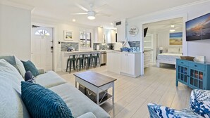 A modern living room with a sofa, a coffee table, and a dining area with chairs. There is a kitchen with a bar and a view of the sea. - Poolside Paradise with Patio, Steps from Beach (St. Pete Beach)