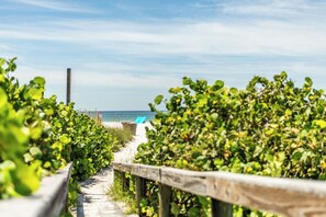 A beach path with a wooden fence, leading to a beach with a blue umbrella.