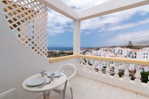 Un balcón con una mesa para dos, con vistas a un pueblo costero de edificios blancos y al mar.
