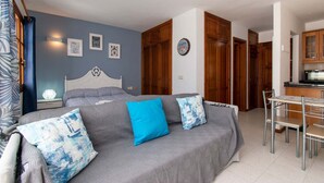 A bedroom with a bed, bedside tables, a desk, and a chair. There are wooden doors and a kitchen area visible. - Terrace View Studio (Costa Adeje)