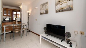 A modern living room with a flat-screen TV, a dining area with a table and chairs, and a kitchen with wooden cabinets and a microwave. - Terrace View Studio (Costa Adeje)