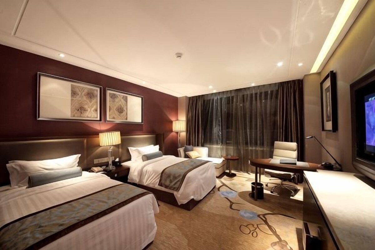 Une chambre d’hôtel avec deux lits, un bureau, une chaise, une télévision et une grande fenêtre avec des rideaux.