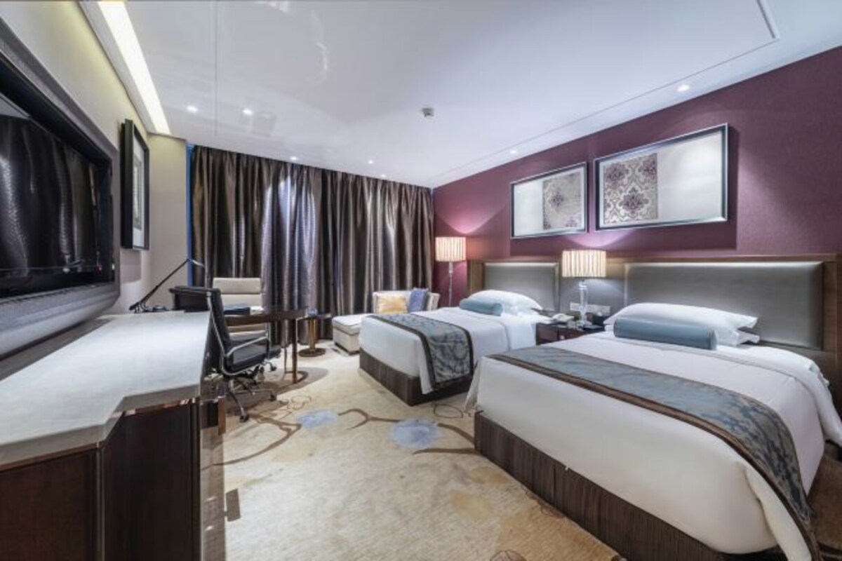 Een hotelkamer met twee bedden, een bureau, een stoel, een televisie en een groot raam met gordijnen.
