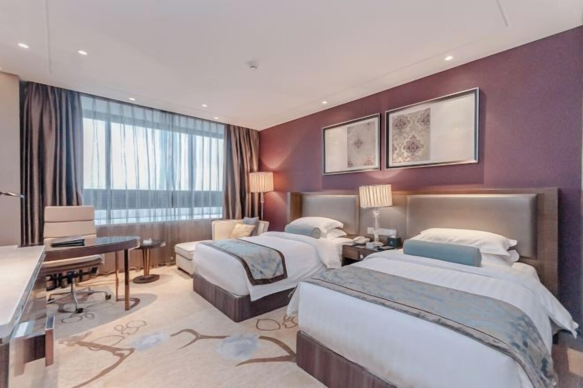 A modern hotel room with two beds, a desk, and a large window with curtains.