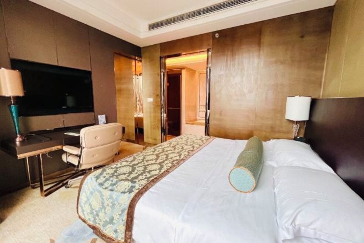 Hotelkamer met een bed, een bureau, een stoel, een televisie en een deur naar een andere kamer.