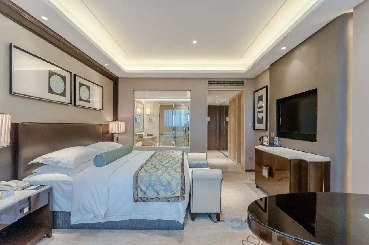 Een moderne hotelkamer met een groot bed, nachtkastjes, een flatscreen televisie en een badkamer met glazen wanden.