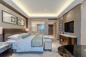 Een moderne hotelkamer met een groot bed, nachtkastjes, een flatscreen televisie en een badkamer met glazen wanden.