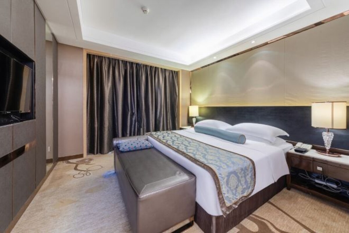 Een moderne hotelkamer met een groot bed, een bankje, een televisie en een bureau met een lamp.
