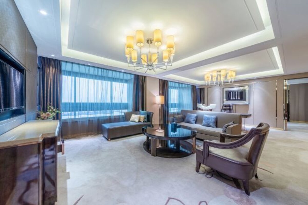 Ruime hotelkamer met een groot bed, een zithoek met een bank en fauteuils, een ronde salontafel en een televisie.