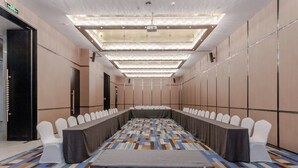 Ein Konferenzraum mit einem langen Tisch, weißen Stühlen und einem gemusterten Teppich.
