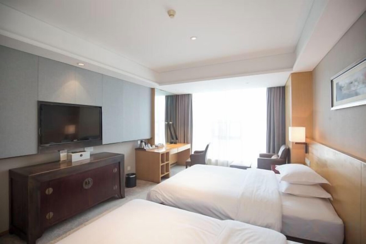 A hotel room with two beds, a desk, a television, and a large window.