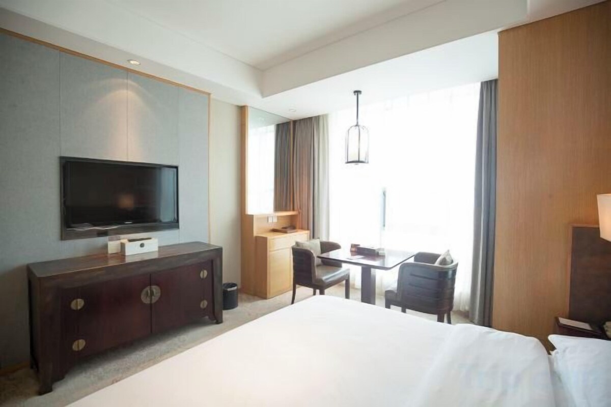 A hotel room with a bed, a TV, a desk, and a chair.