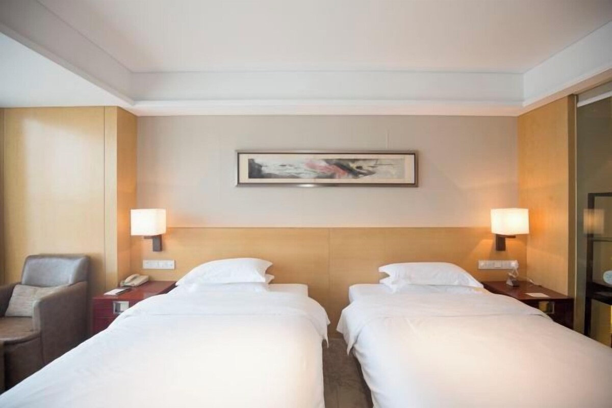 Een hotelkamer met twee eenpersoonsbedden, een stoel, een bureau met een lamp en een schilderij aan de muur.