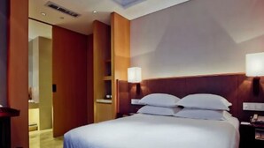Una habitación de hotel con una cama grande, mesitas de noche y una mesita auxiliar.
