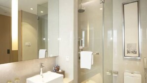 Un baño moderno con un espejo grande, un lavamanos blanco, una ducha con mampara de vidrio y un inodoro.