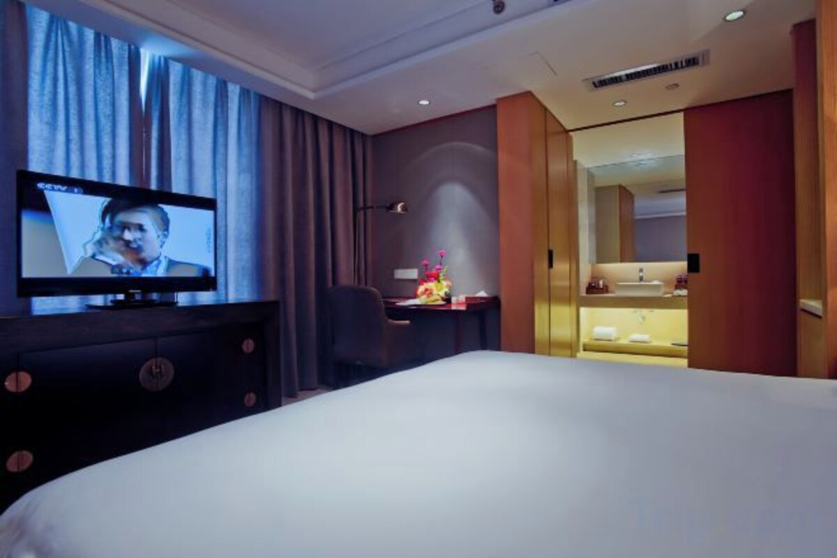 A hotel room with a bed, a desk with a television, a chair, and a bathroom visible through an open door.