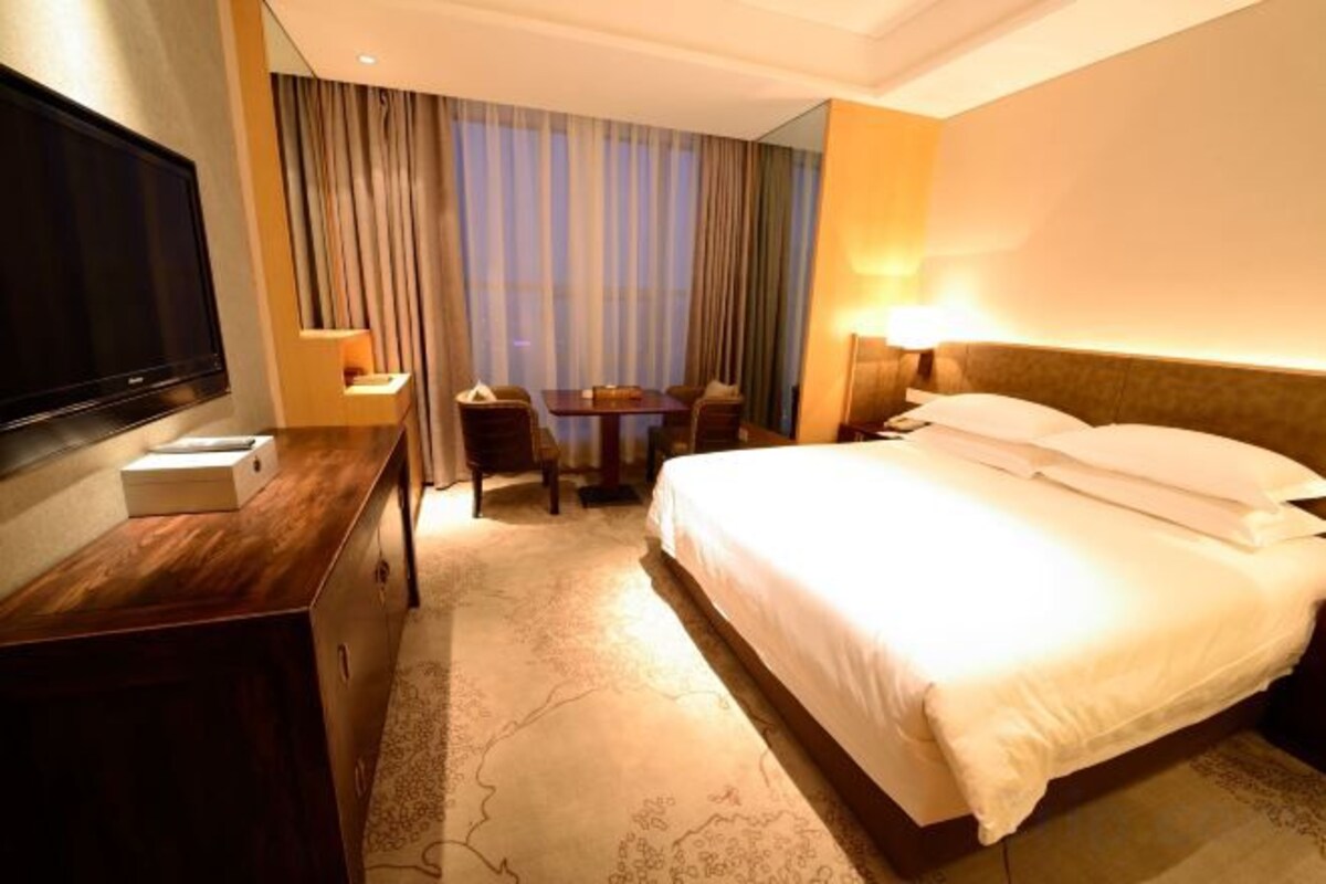 A hotel room with a bed, a desk, a television, a table, and a chair.