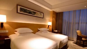 Habitación de hotel con dos camas, una mesita de noche, una lámpara, una silla y un amplio ventanal con cortinas.