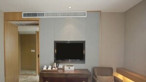 Habitación de hotel con televisor de pantalla plana en la pared, un mueble de madera con cafetera y un sofá.