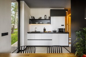 Una cocina moderna con armarios blancos, encimeras negras y salpicadero negro. Hay una zona de comedor con una mesa y sillas de madera.