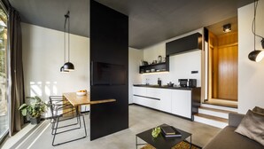 Une cuisine moderne avec un réfrigérateur noir, des armoires blanches et un plan de travail en bois. On y trouve un coin repas avec une table et des chaises, ainsi qu’un canapé dans le salon.