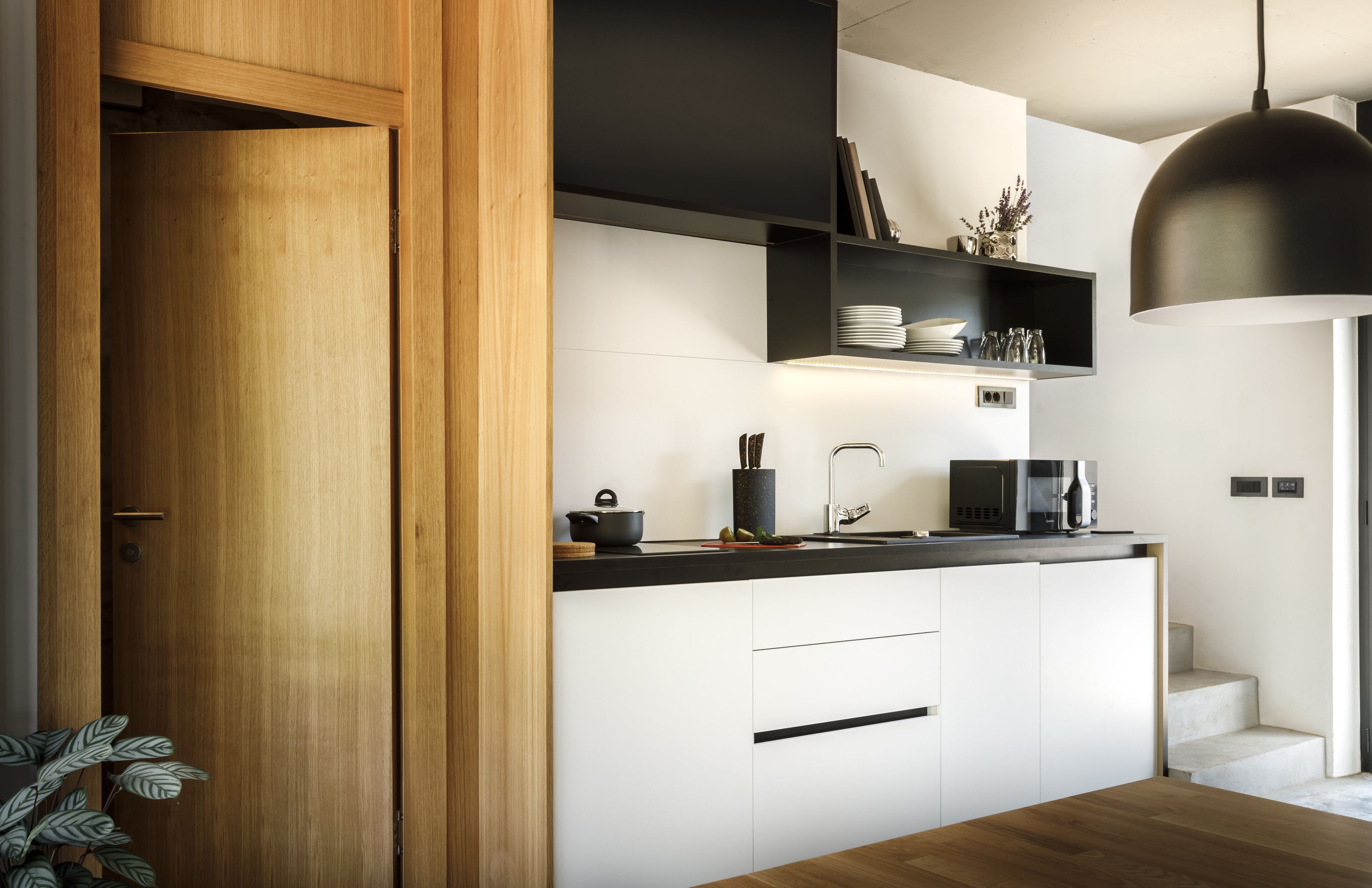 Une cuisine moderne avec des armoires blanches, un plan de travail noir et une porte en bois.