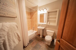 A bathroom with a bathtub, sink, and toilet. There is a shower curtain, a towel, and a mirror above the sink. - Red Hawk Lodge 2211 (Keystone)