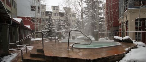 A snow-covered outdoor area with a hot tub, steps, and a brick wall.