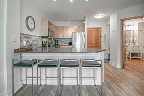 A modern kitchen with a central island, stainless steel appliances, and a wooden door leading to a bathroom.