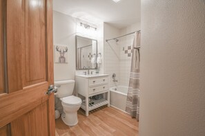Ein Badezimmer mit Holztür, weißen Sanitärobjekten, Toilette, Waschtisch und sowohl Badewanne als auch Dusche.