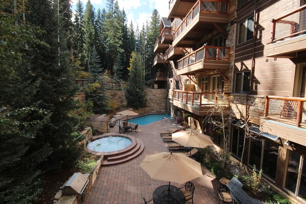Relax in a hot tub surrounded by a tranquil forest view, with a pool and lounge chairs nearby.
